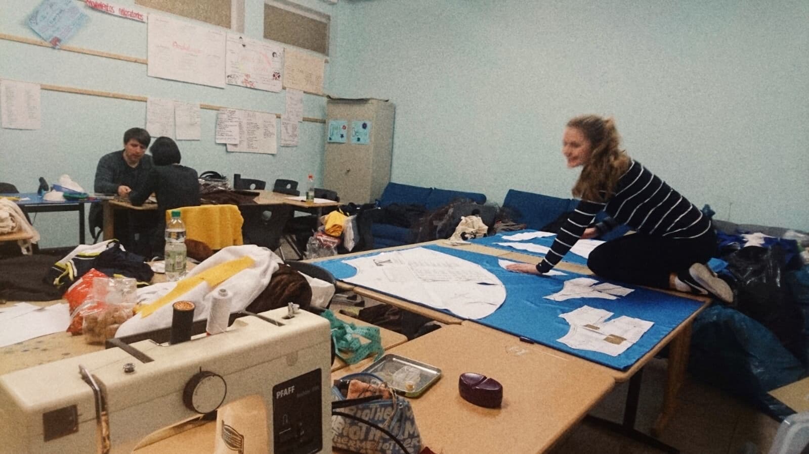 Im Zentrum steht ein großer Tisch mit vielen Kostümschablonen und Nähmaschienen.