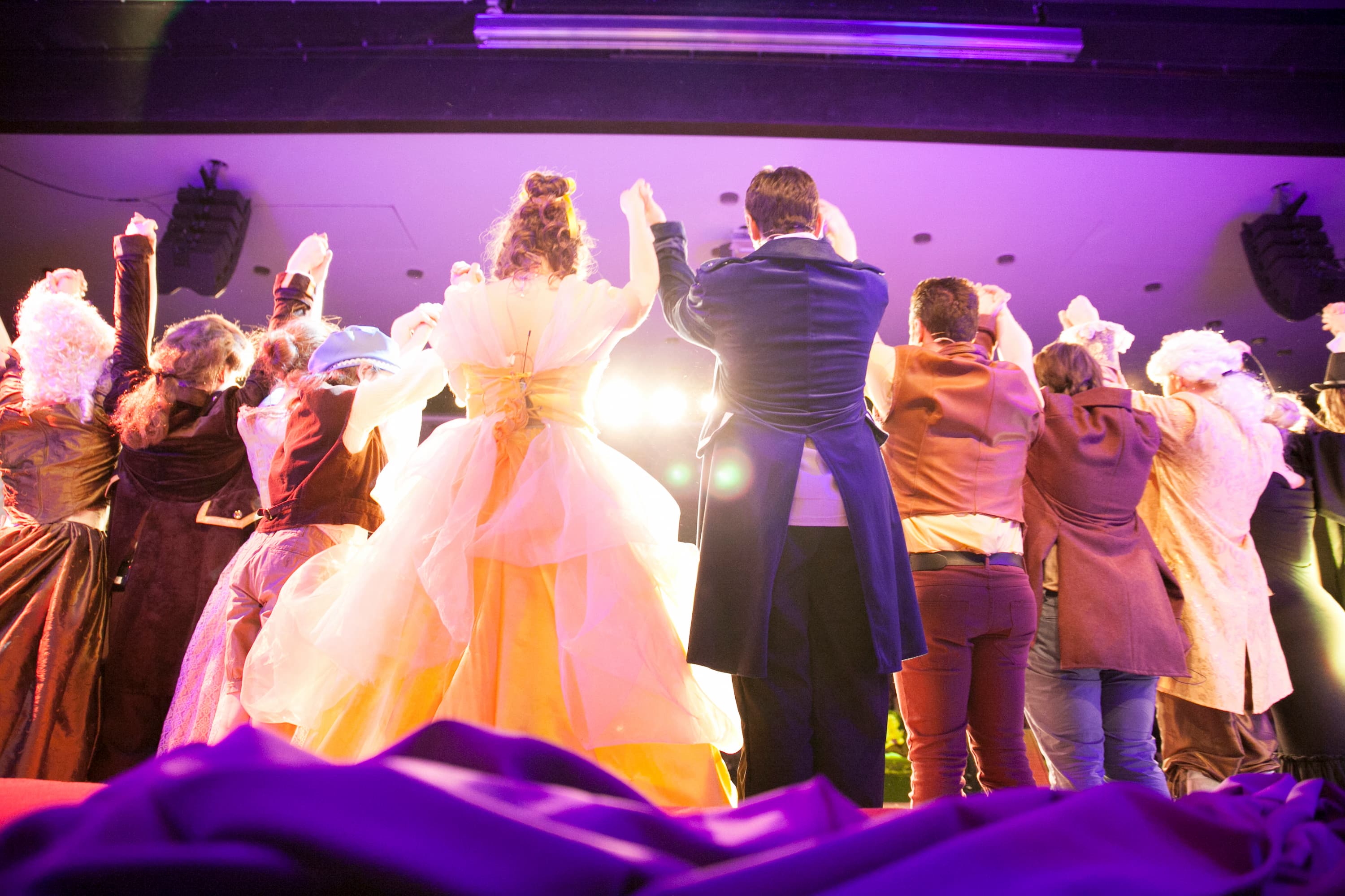 Mehrere Darsteller in Kostümen verbeugen sich. Sie sind von hinten zusehen.