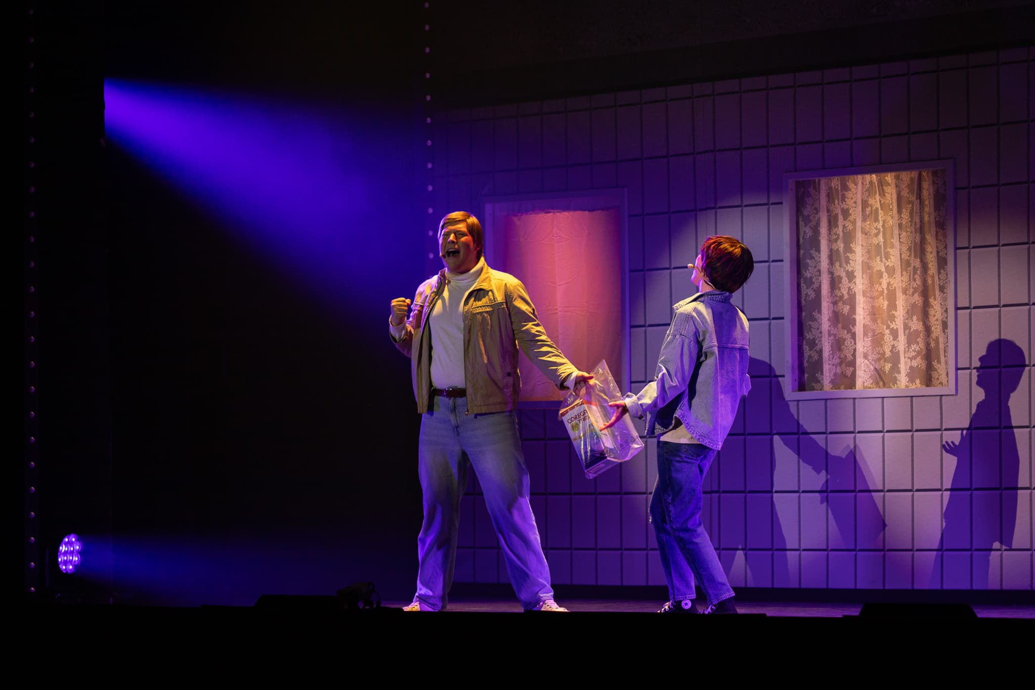 Zwei Personen stehen sich auf einer Bühne gegenüber und singen sich an. Im Hintergrund steht eine Häuserwand.