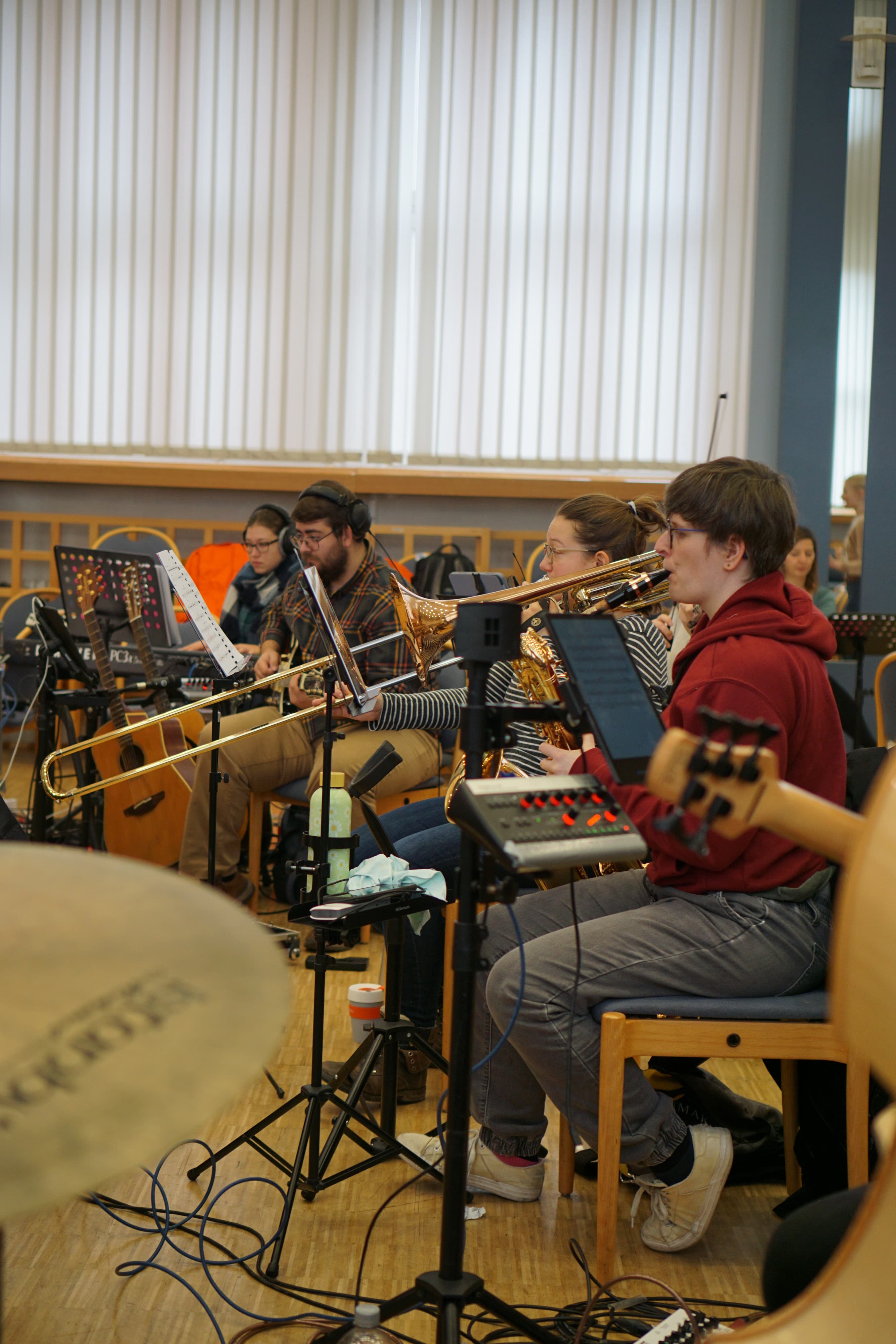 Orchesterprobe mit Blechbläsern und Gitarren, Musiker spielen nach Noten im Proberaum