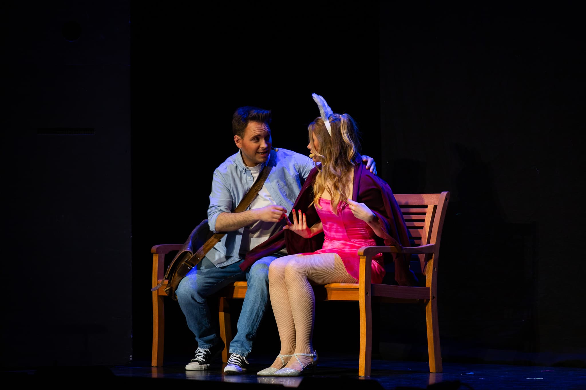 Mann und Frau sitzen auf Bank, sprechen miteinander; die Frau trägt pinkes Kleid und Hasenohren.