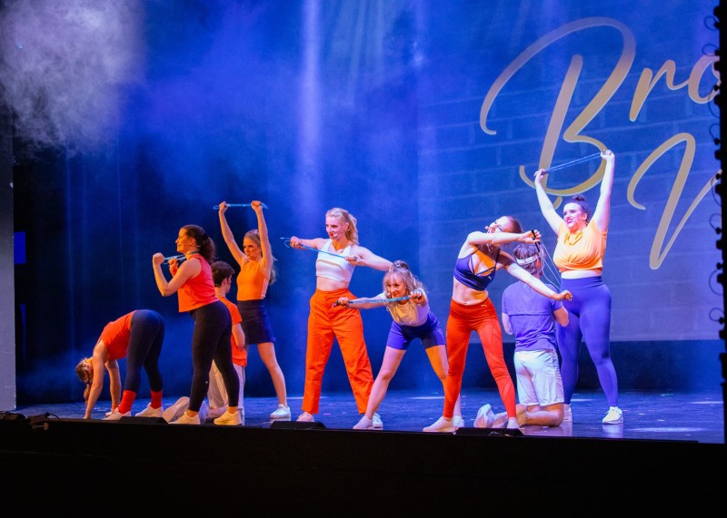 Tanzgruppe in Sportoutfits führt Choreografie mit Springseilchen aus, Bühnenlicht in Blau und Orange.