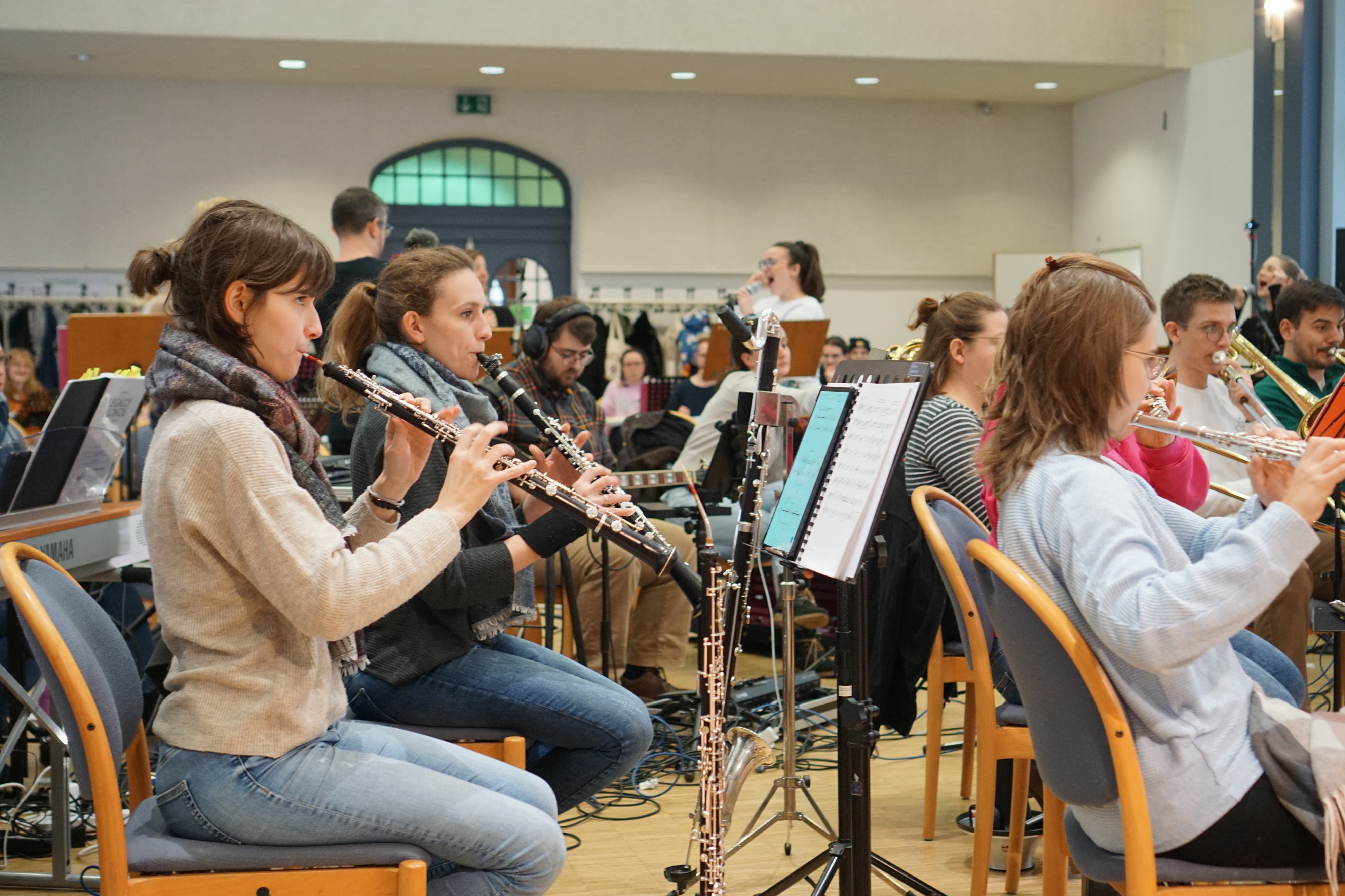 Orchesterprobe mit mehreren Musikerinnen und Musikern, Holzbläser spielen nach Noten im Raum