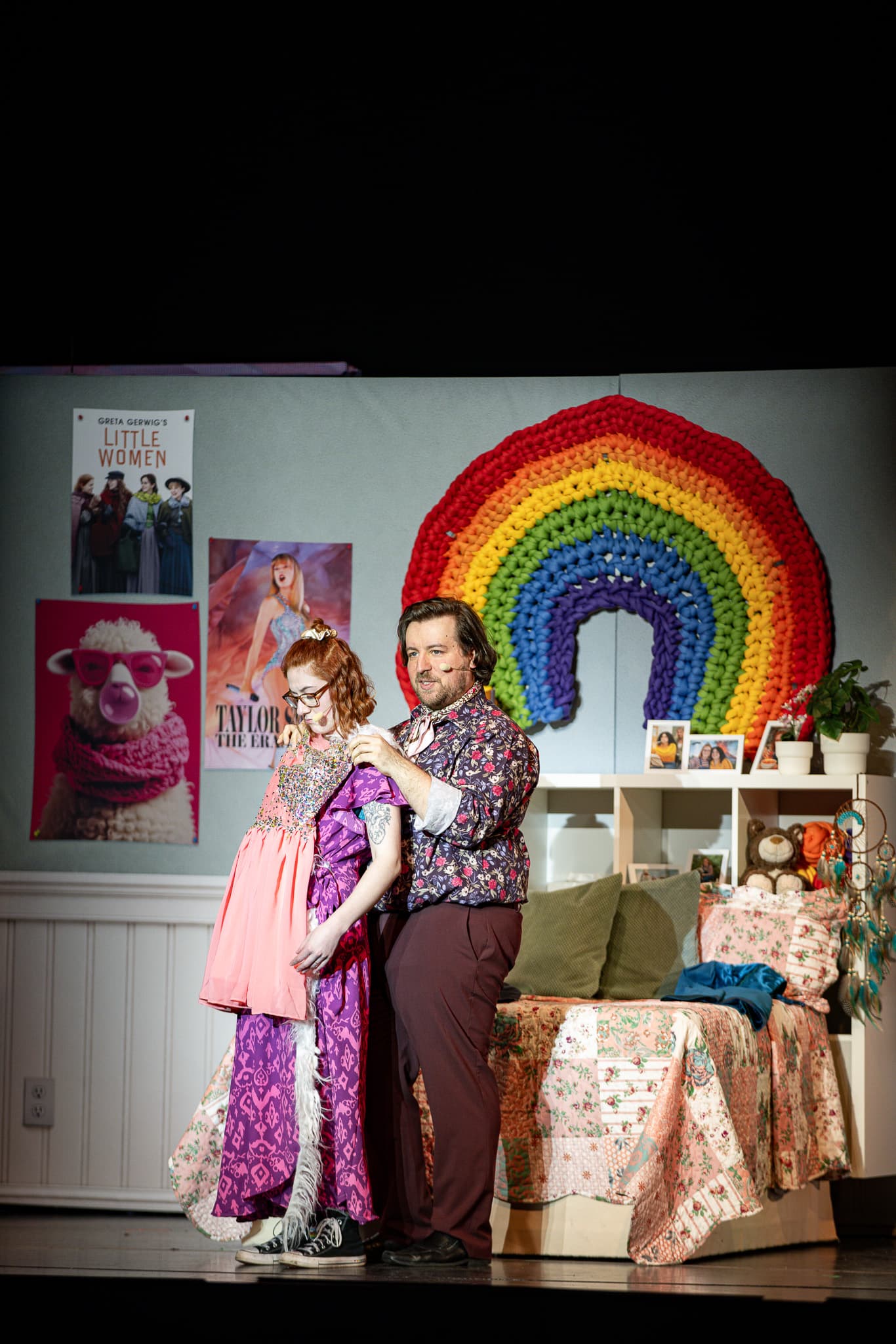 Eine Person hilft einer anderen beim Ankleiden in einem Zimmer mit Regenbogen-Dekoration und Postern an der Wand.