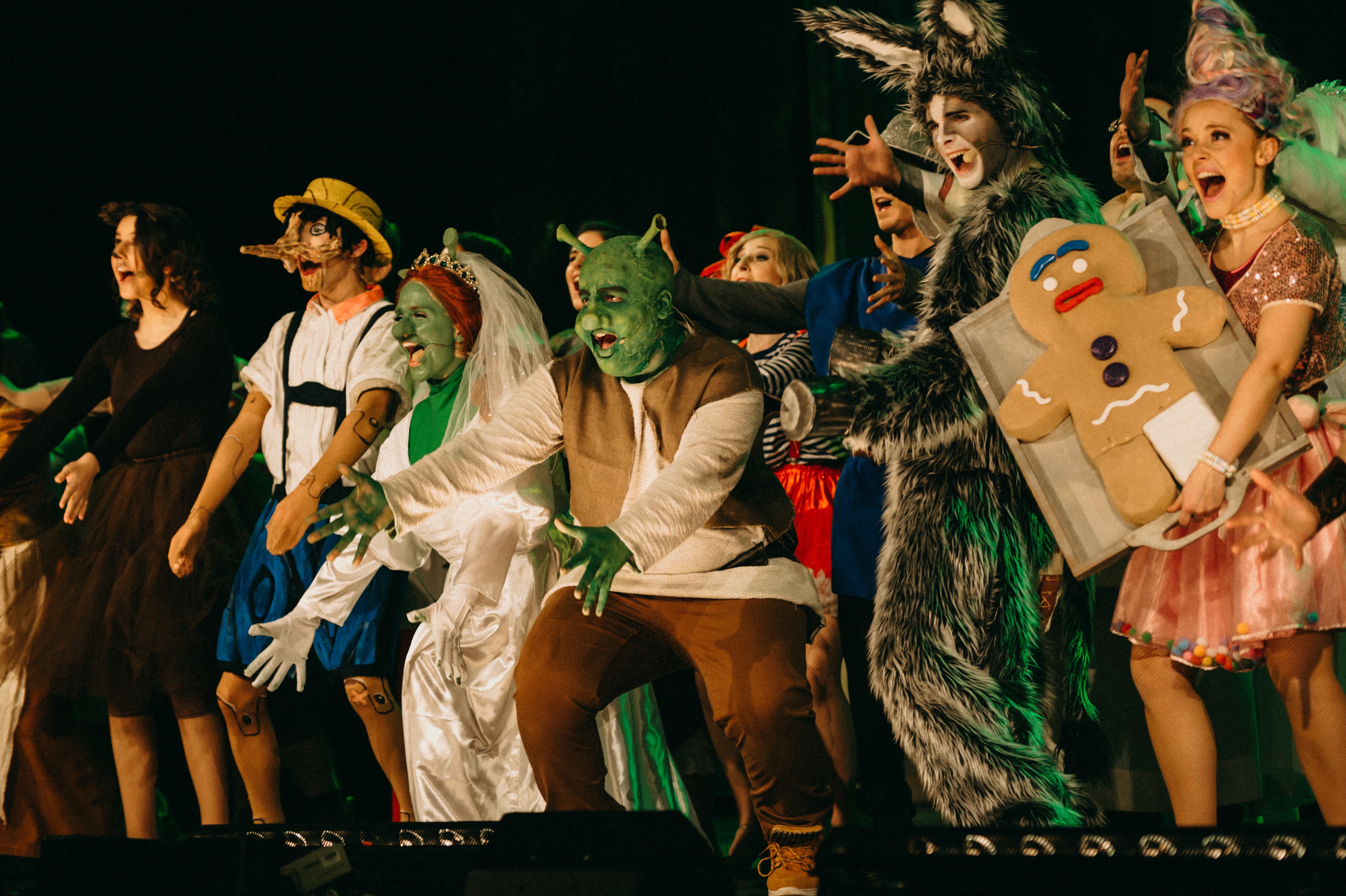Eine Gruppe an Darsteller steht kostümiert nebeneinander und strahlt in das Publikum. Zu sehen sind er hölzerne Pinocchio, die Oger Fiona und Shrek, der Esel und die Zuckerfee mit einer großen Kecks-Figur.