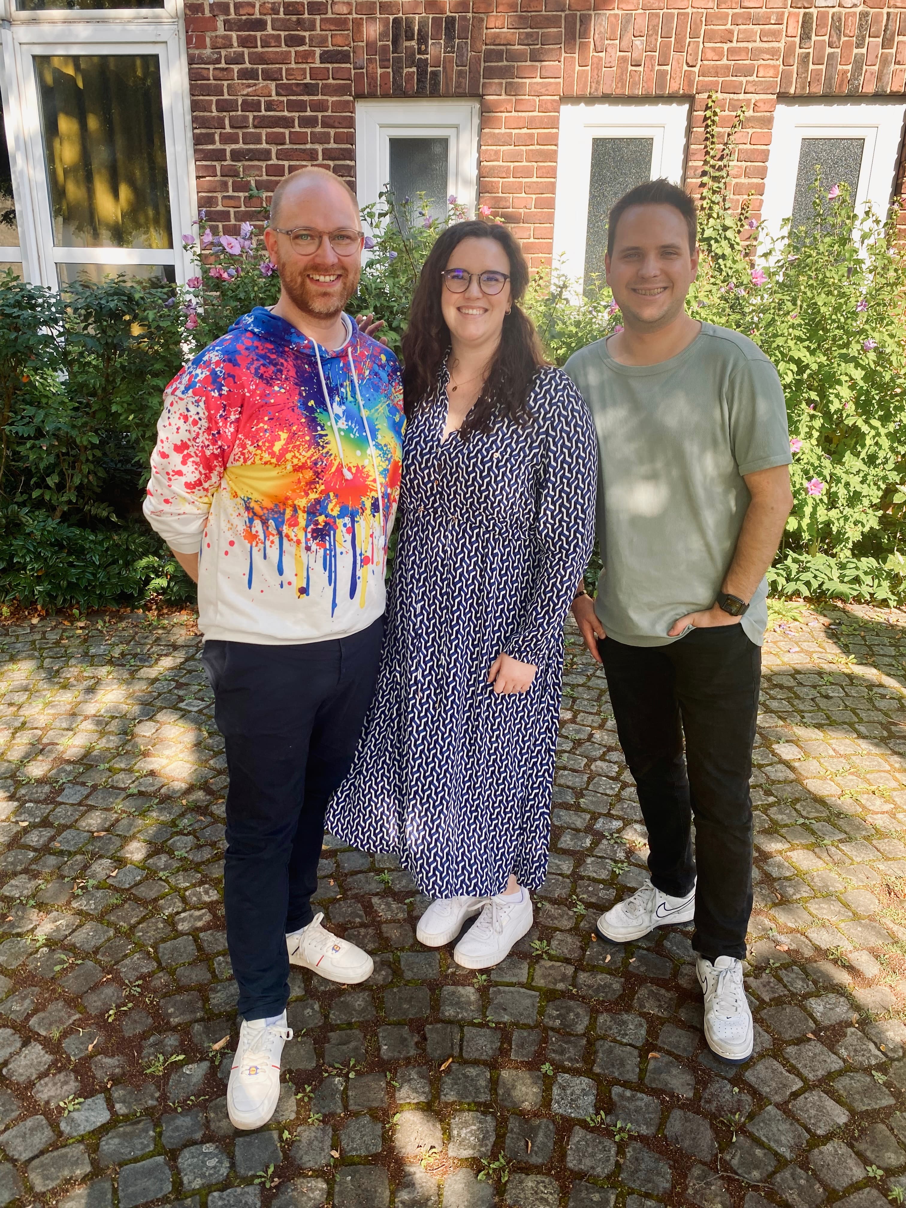 Drei Menschen stehen lächelnd vor einer Hauswand