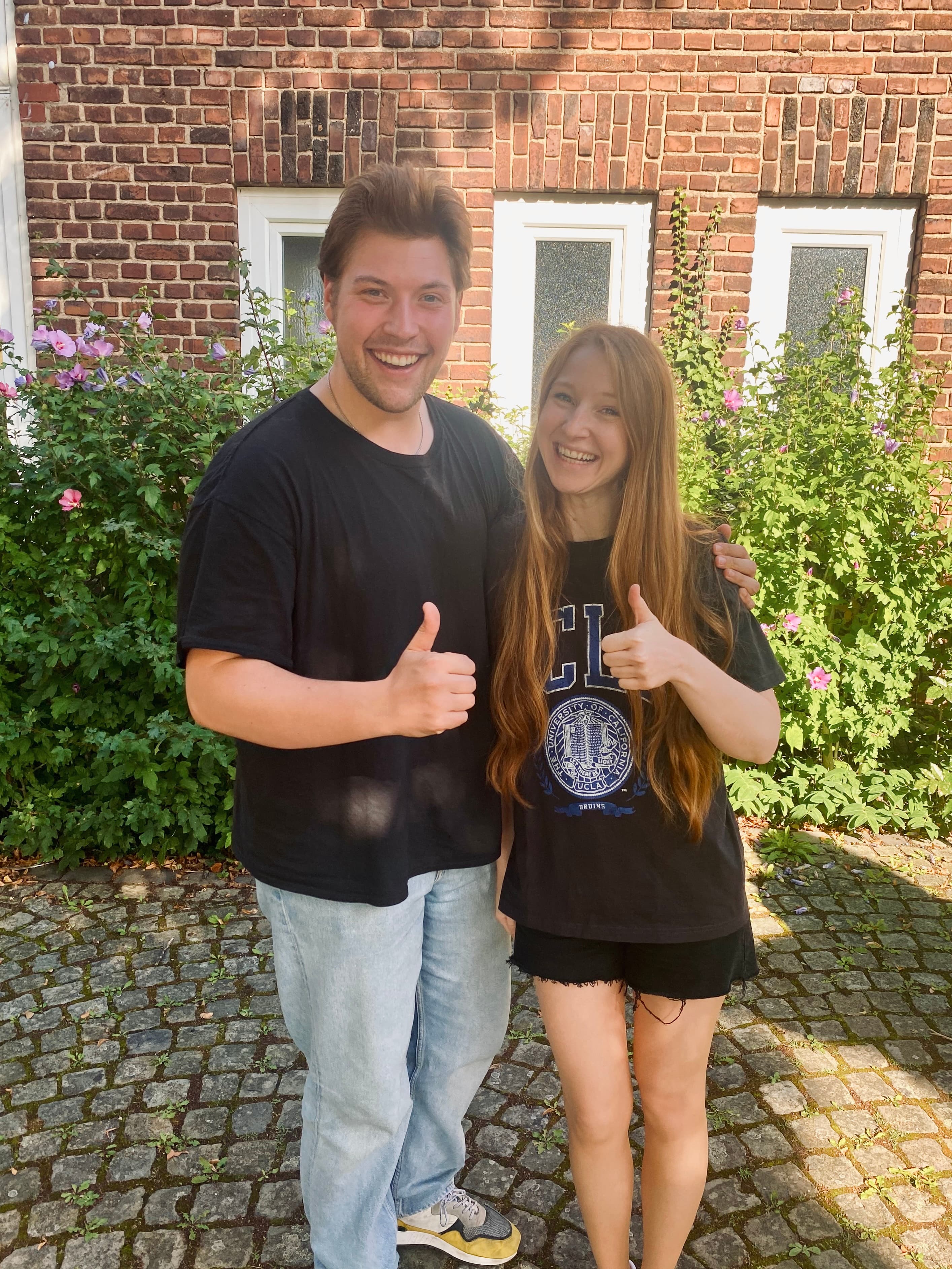 Ein Mann und eine Frau stehen nebeneinaner lächelnd vor einer Hauswand.