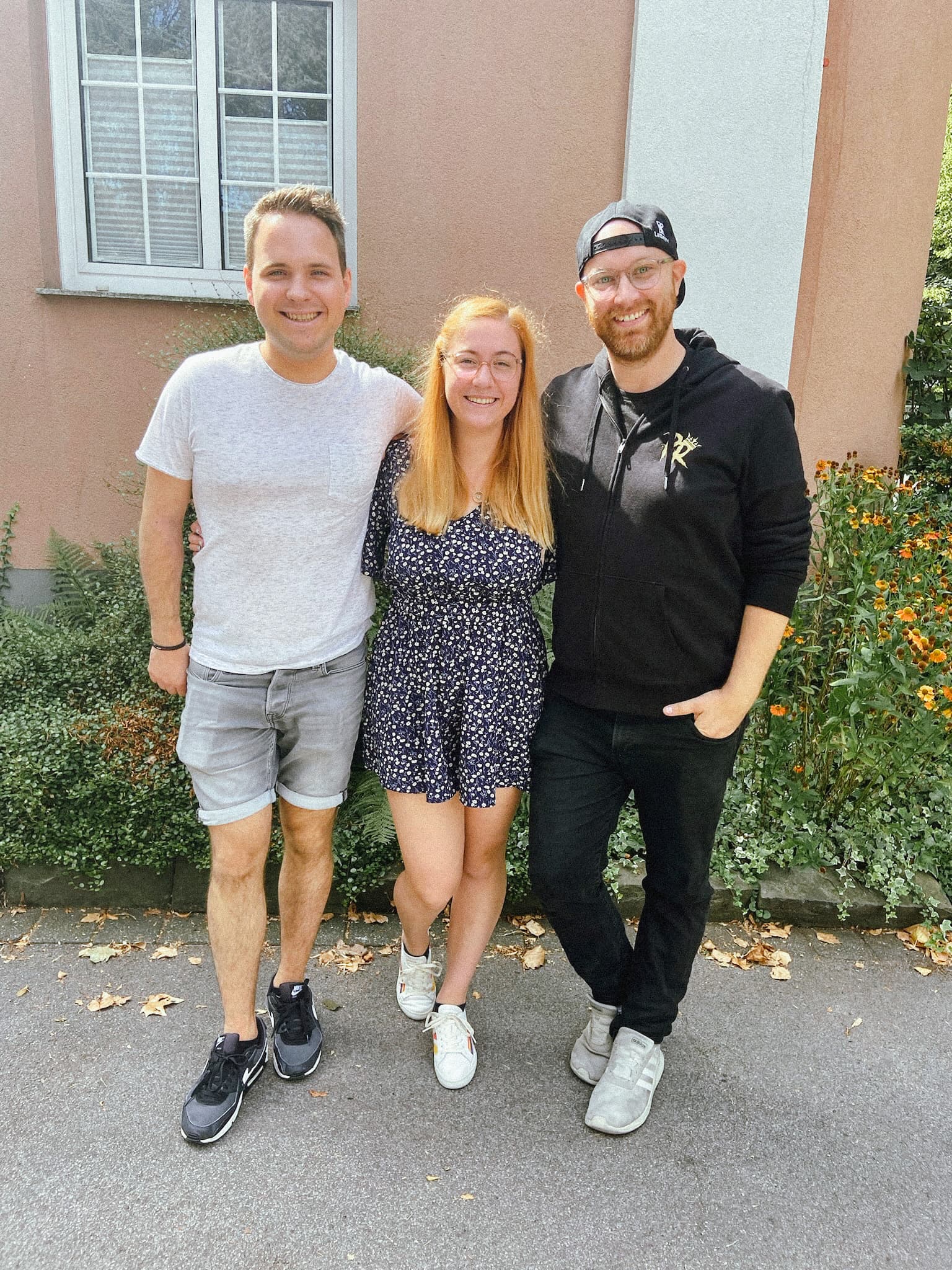 Drei Personen stehen lächelnd nebeneinander