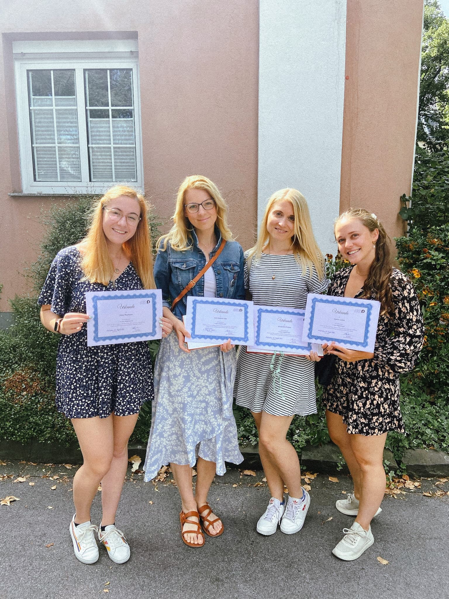 Vier Frauen in Sommerkleidern stehen lächelnd vor einem Haus und halten Urkunden in der Hand