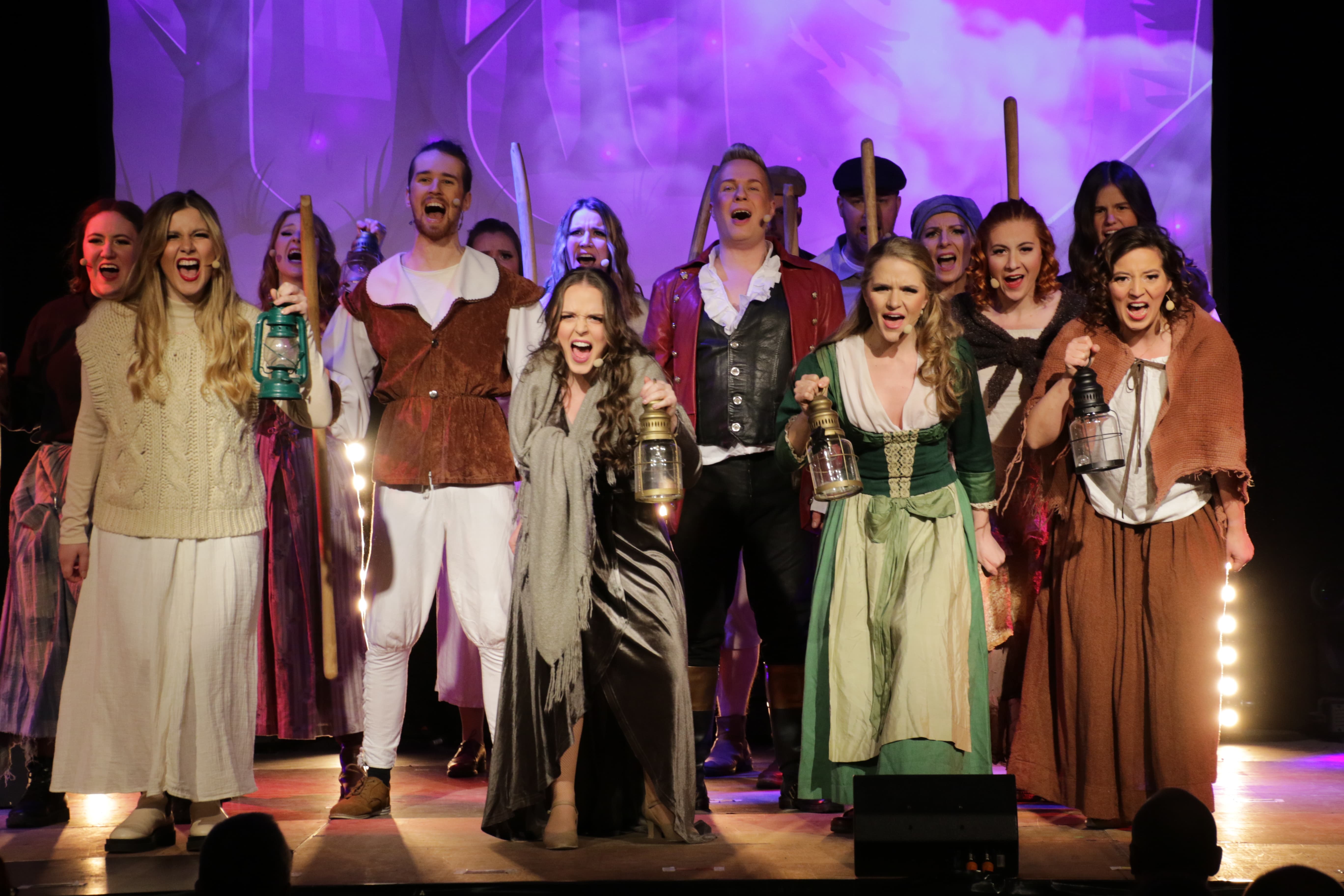 Eine große Gruppe in Dorfbekleidung steht mit Laternen und Mistgabeln in der Hand nebeneinander und singt in das Publikum.