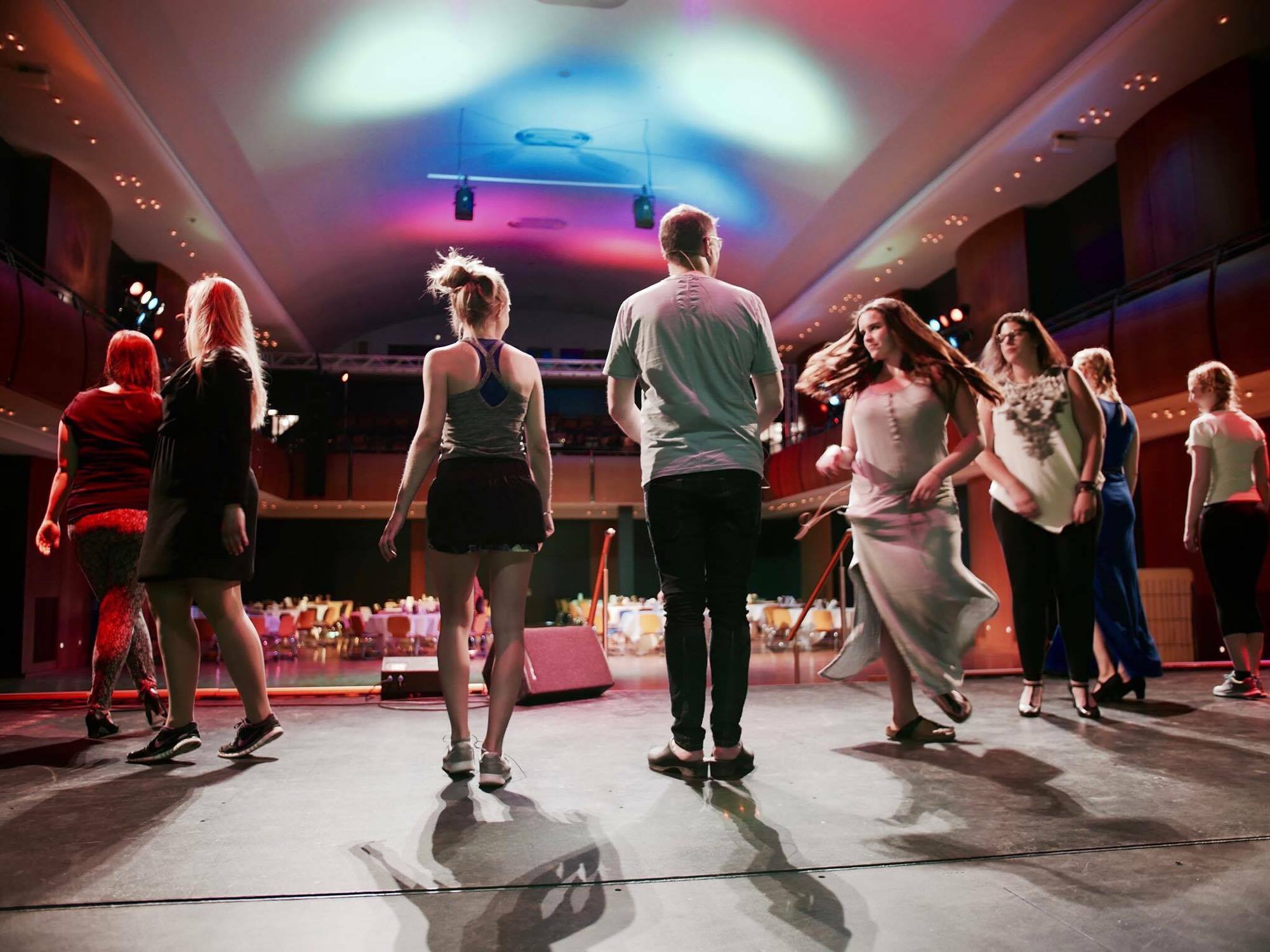 Mehrere Darsteller stehen auf der Bühne. Blick von hinten auf den Zuschauerbereich.