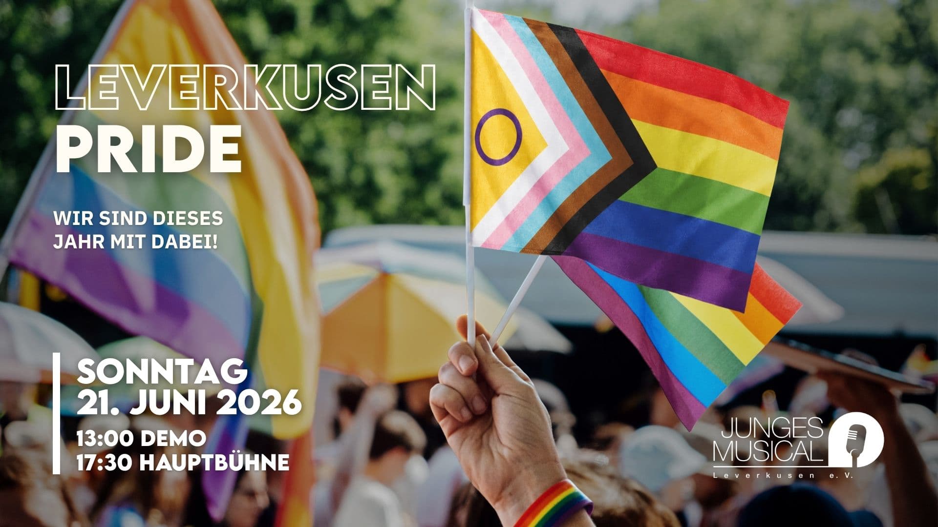Pride-Flaggen in der Hand vor Parade-Hintergrund: „Leverkusen Pride – wir sind dabei! So. 21.6., 13:00 Demo, 17:30 Bühne.“