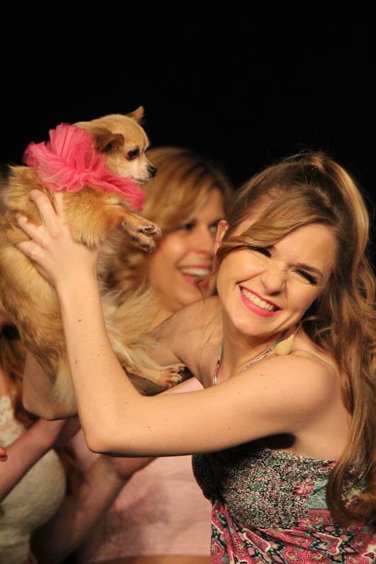 Eine blonde Frau hält lächelnd einen kleinen Hund in die Höhe.